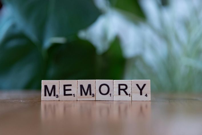 Wooden letter tiles spelling 'Memory' on a wooden table with blurred green background.