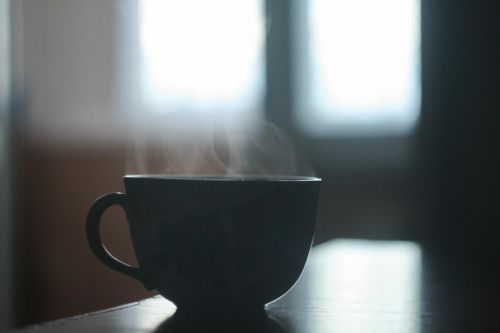 A close-up of a steaming mug of coffee on a table with soft backlight, creating a cozy morning ambiance.