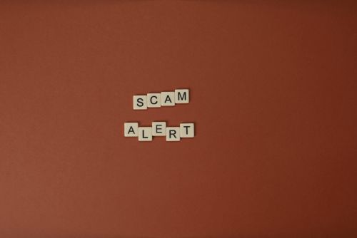 Scrabble tiles spelling Scam Alert on a brown surface indicating caution.