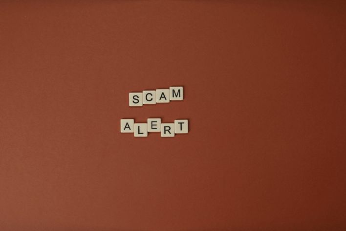 Scrabble tiles spelling Scam Alert on a brown surface indicating caution.