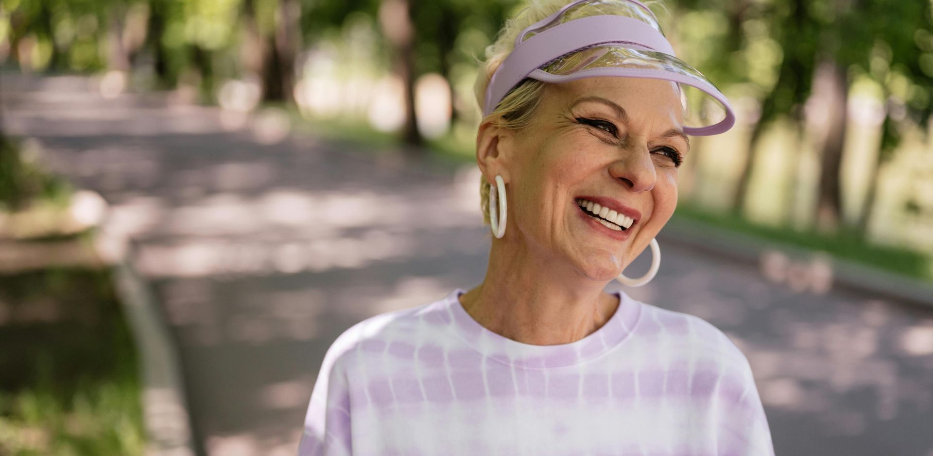 Smiling elderly woman enjoying a sunny day outdoors wearing a stylish sun visor.