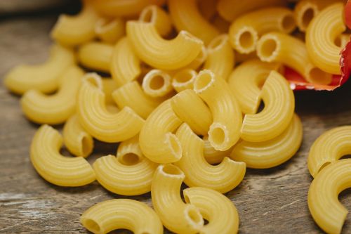 From above heap of pipe rigate pasta scattered on wooden table from opened pack in kitchen