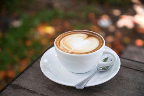 A beautifully crafted latte with heart art sits on a wooden table outdoors.
