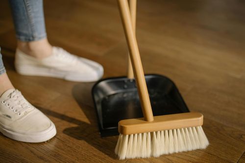 Close-up of cleaning process with broom and dustpan beside sneakers on a wooden indoor floor.
