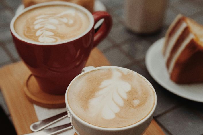 Delicious latte art accompanied by a slice of cake on a cafe table.